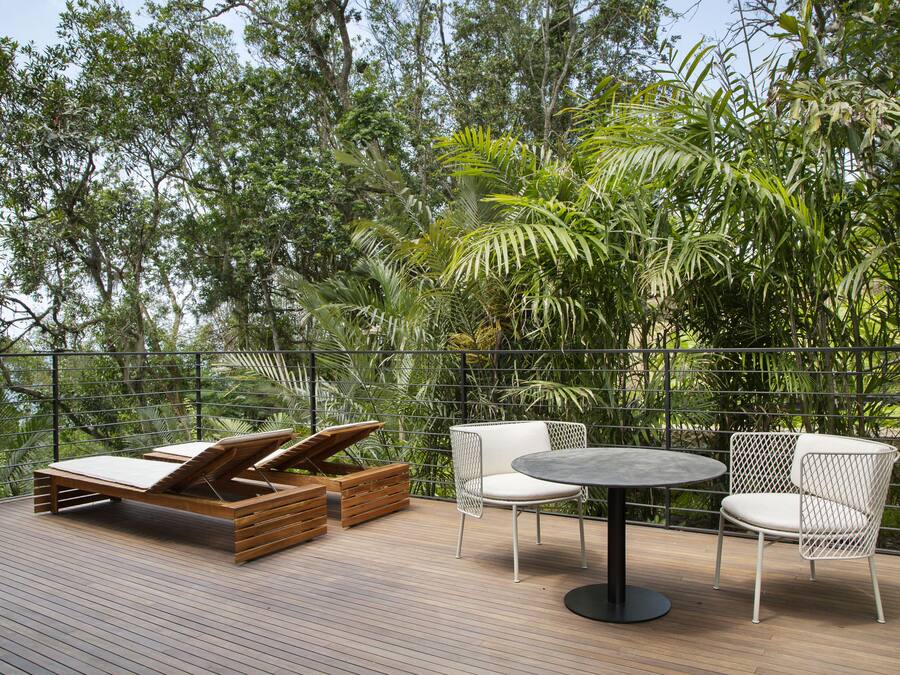 Una terraza de madera con una silla de descanso, dos sillas blancas y una mesa redonda.