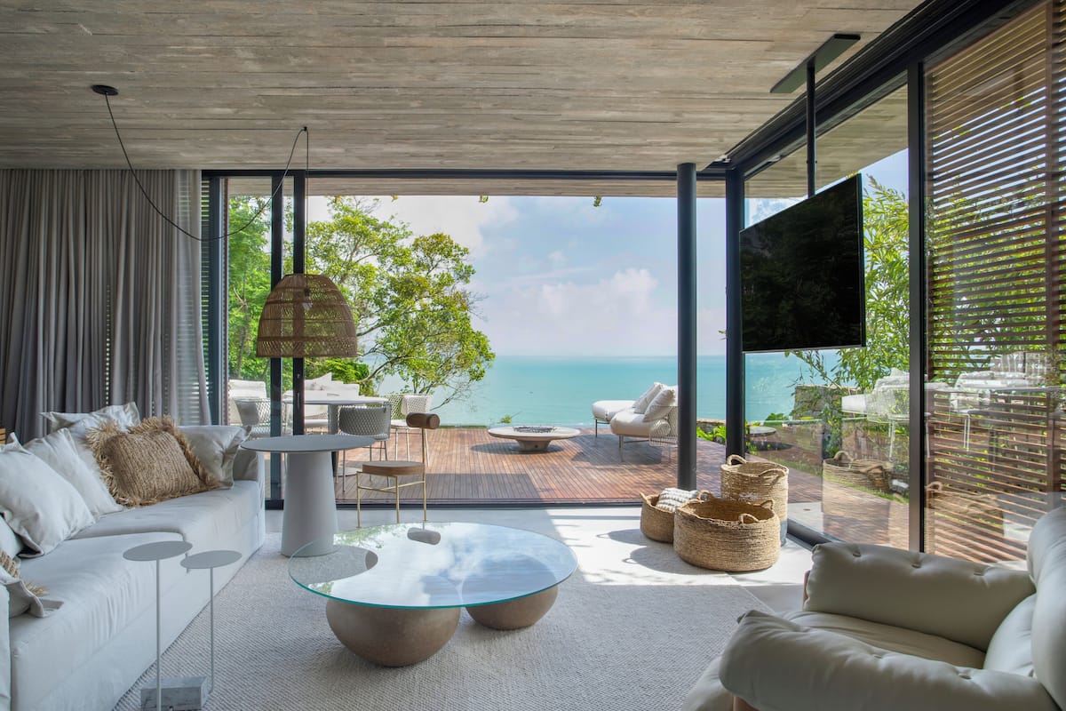 A modern living room with a glass coffee table, white sofas, and a view of the ocean.