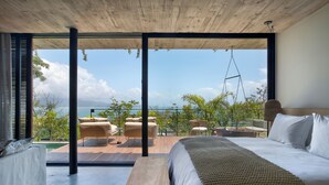 A bedroom with a large bed, a wooden bench, and a view of the ocean through floor-to-ceiling windows. - Fuso Concept Hotel (Florianópolis)