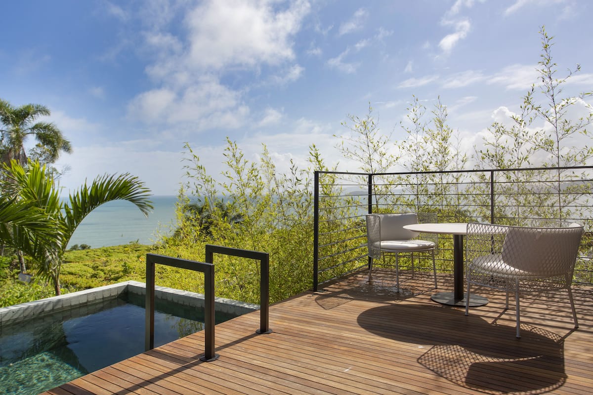 A wooden deck with a pool, outdoor furniture, and a view of the ocean.