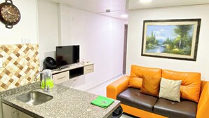 A modern kitchen with a granite countertop, built-in cabinets, and a sink. There is a small island with a green towel and a knife. A brown leather sofa with orange cushions is against the wall, and a painting is above it. - Apartahotel222 Apto 401 (Pereira)