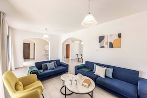 Uma sala de estar moderna com dois sofás azuis, uma poltrona amarela, uma mesa de centro e arte abstrata nas paredes.