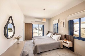 Quarto com duas camas, uma mesa de cabeceira, luminária pendente, janela com cortinas e vista para o exterior.