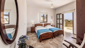 Ein Schlafzimmer mit zwei Betten, einem großen Spiegel, Nachttischen mit Lampen, einer Topfpflanze und einem Balkon mit Blick.