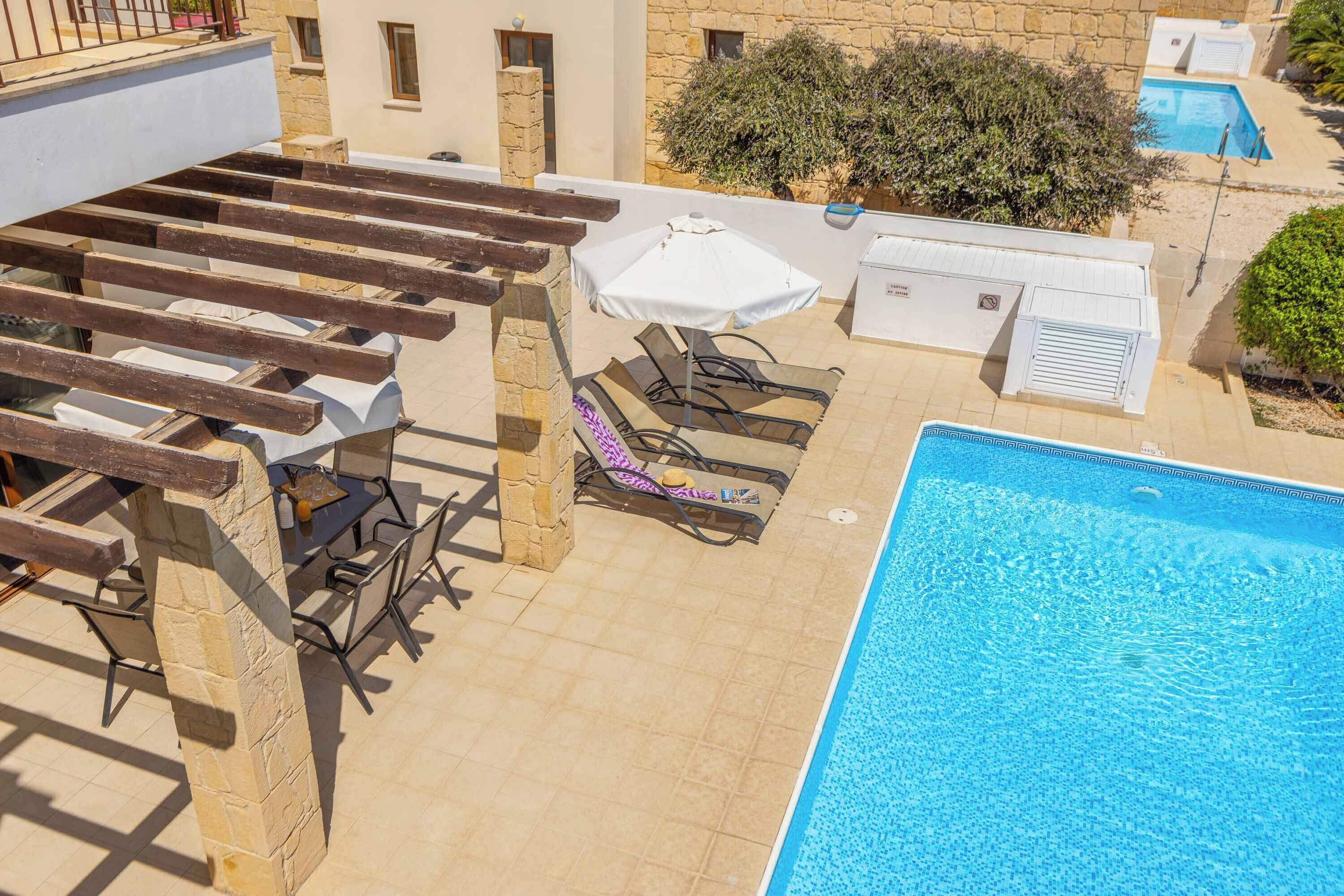 A rooftop pool area with lounge chairs and an umbrella, surrounded by stone walls and vegetation.