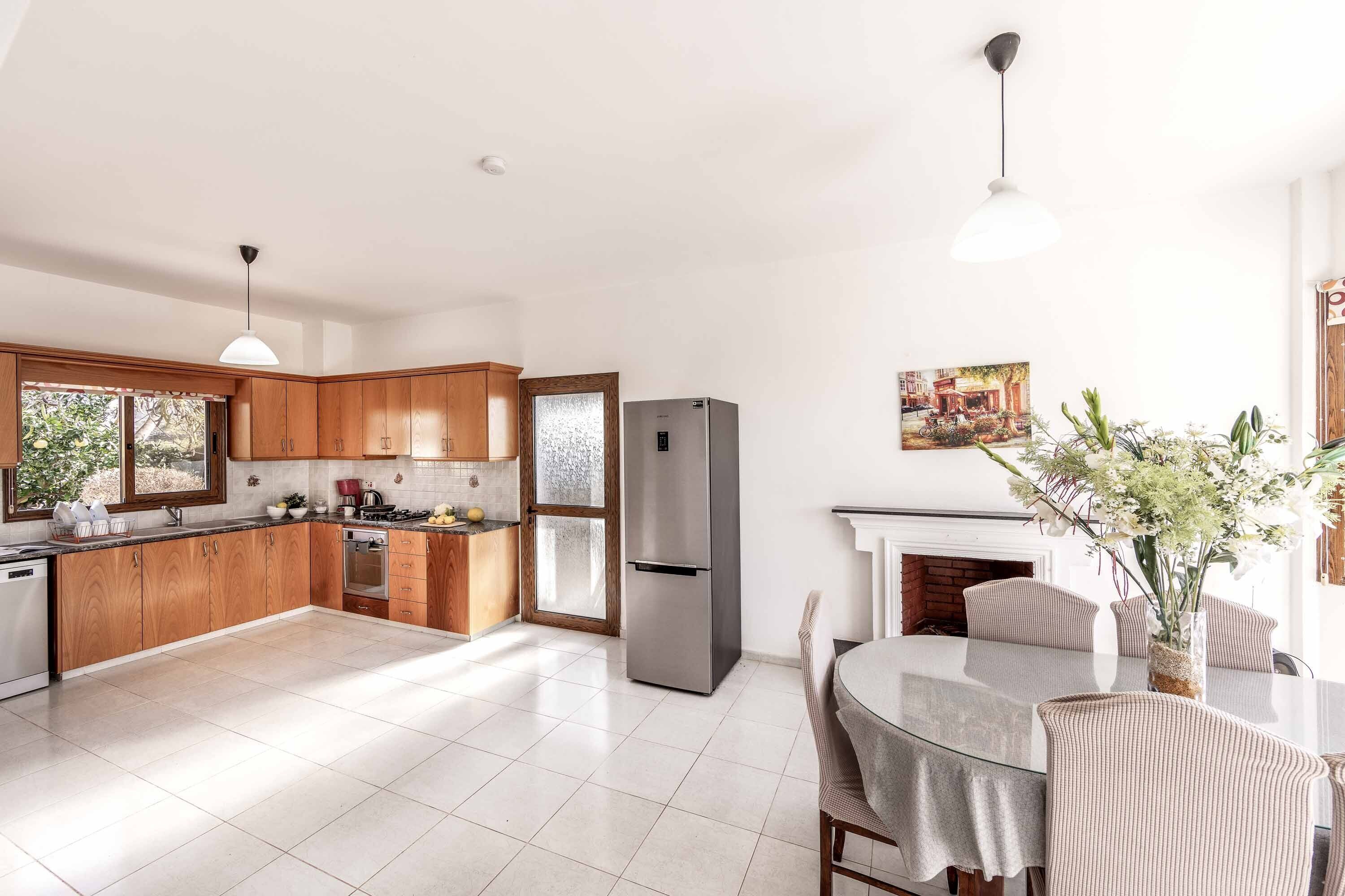 Una cocina moderna con armarios de madera, un refrigerador de acero inoxidable y una zona de comedor con una mesa de vidrio y sillas a rayas.