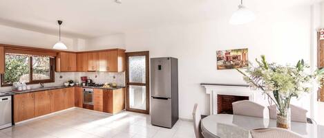 Una cocina moderna con armarios de madera, un refrigerador de acero inoxidable y una zona de comedor con una mesa de vidrio y sillas a rayas.