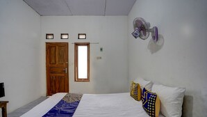 Une chambre à coucher avec un lit, une porte en bois, une fenêtre et un ventilateur fixé au mur.