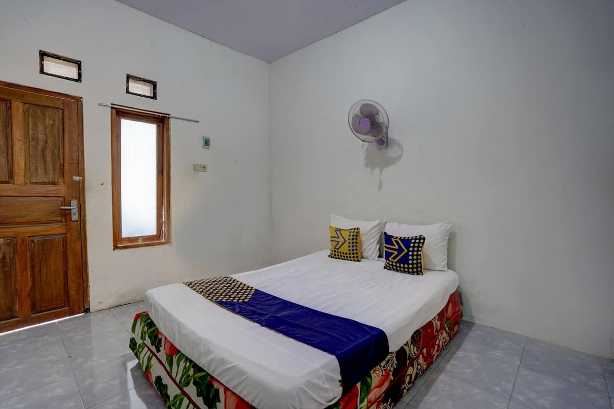 Une chambre à coucher avec un lit, une porte en bois, une fenêtre et un ventilateur fixé au mur.
