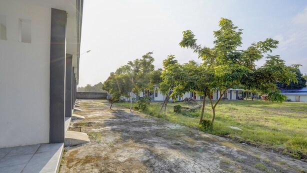 Une cour avec un chemin pavé, des arbres et un bâtiment doté d’un toit plat.
