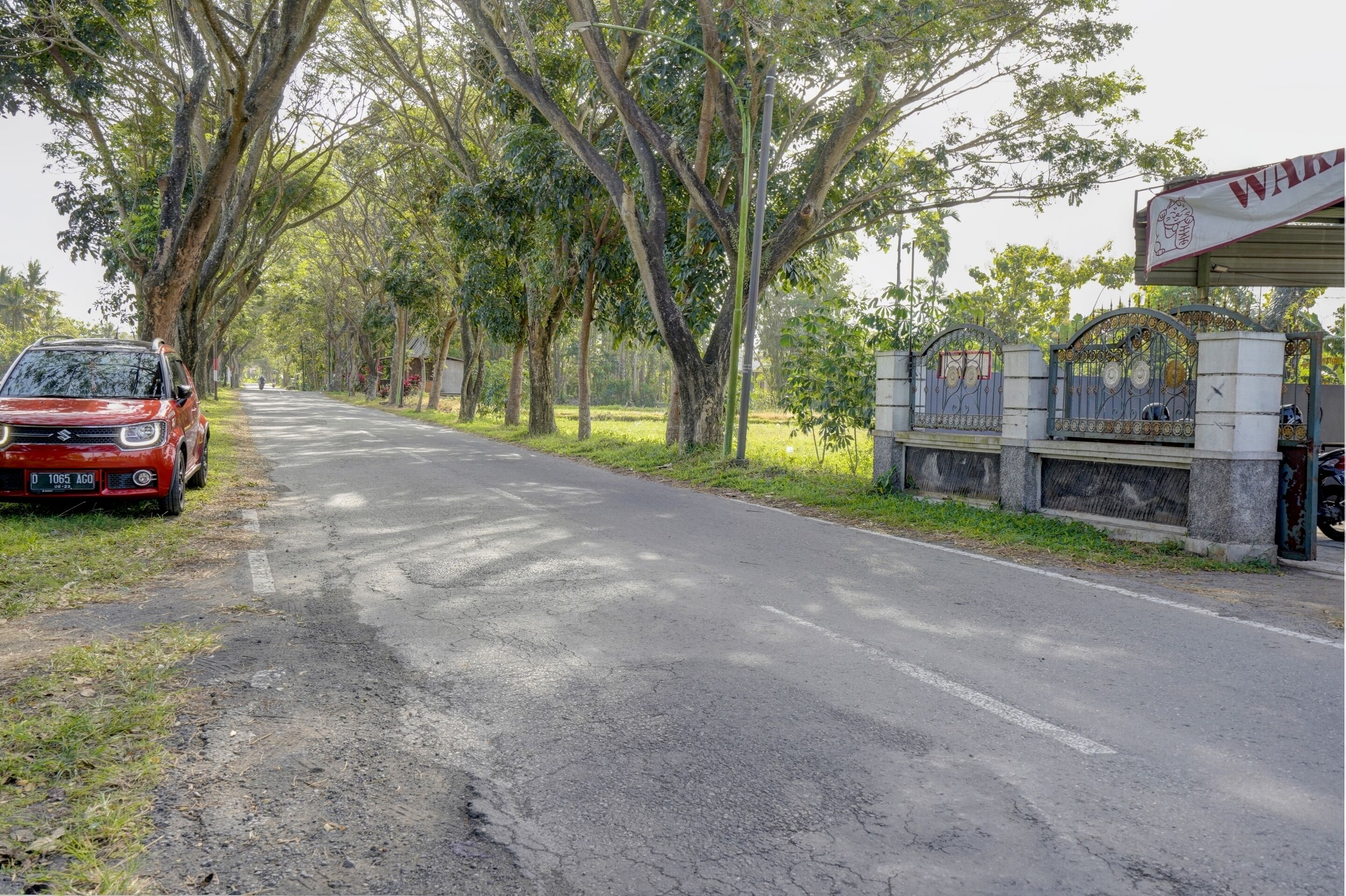 A red car parked on a tree-lined road with a gated entrance and a sign that reads "WARM."