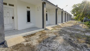 Une rangée de bâtiments blancs avec des portes numérotées, un chemin pavé et un arbre sur la droite.