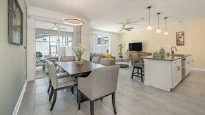 A modern kitchen with a dining area, featuring a central island, pendant lighting, and a large window providing natural light. - Storey Lake-Disney Pool Townhome FREE Water Park (Kissimmee)
