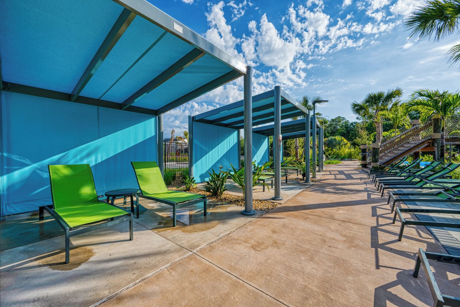 Een overdekt buitengebied met groene lounge fauteuils en een heldere blauwe lucht.