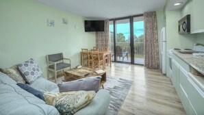 Un salon avec un canapé, une table basse et un téléviseur. Il y a un balcon avec vue.