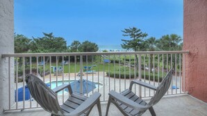 Un balcon avec deux chaises en bois, une piscine et une vue sur l’océan et une plage.