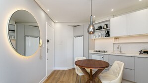 A modern kitchen with white cabinets, a round wooden table, and two white chairs.