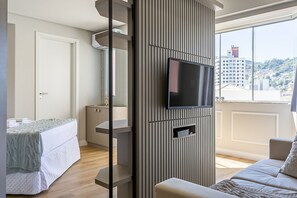 Habitación de hotel moderna con un ventanal grande, un televisor de pantalla plana montado en la pared, una cama con cubierta acolchada y un sofá con una manta estampada.