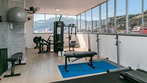 A gym with exercise equipment, a large exercise ball, and a view of a city and hills.