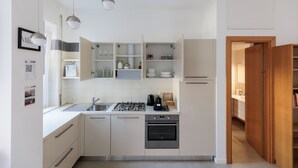 A modern kitchen with white cabinets, a gas stove, and a built-in oven. There are hanging lights and a wooden door leading to another room. - Milan Hub - Sempione, Citylife, MiCo (Milano)