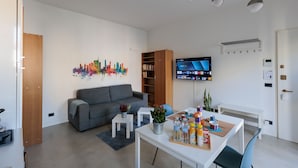 A modern living room with a grey sofa, a coffee table with drinks, a bookshelf, and a TV on the wall. - Milan Hub - Sempione, Citylife, MiCo (Milano)