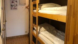 Habitación con literas, una escalera de madera, un cartel en la pared y un respiradero blanco en el techo.