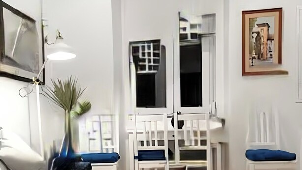 Una sala de estar moderna con un sofá negro, una mesa de comedor blanca con sillas y un ventanal grande.