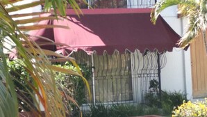 A building with a red awning, a metal gate, and a small garden area with yellow flowers. - Tranquille2, Jamaica vacation Kingston/St. Andrew
 (Kingston)