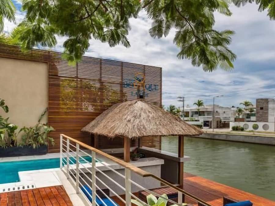 Un área junto a la piscina con cubierta de madera, sillas de descanso y una sombrilla de paja.
