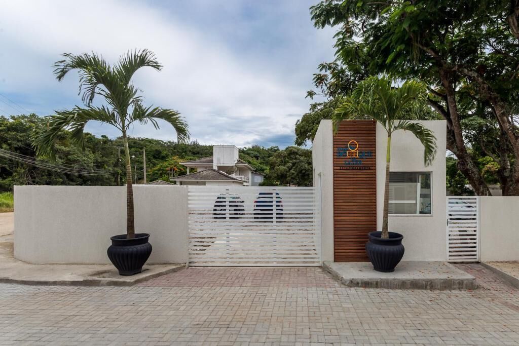 Uma entrada com portão, um edifício moderno, palmeiras e um caminho de acesso pavimentado.