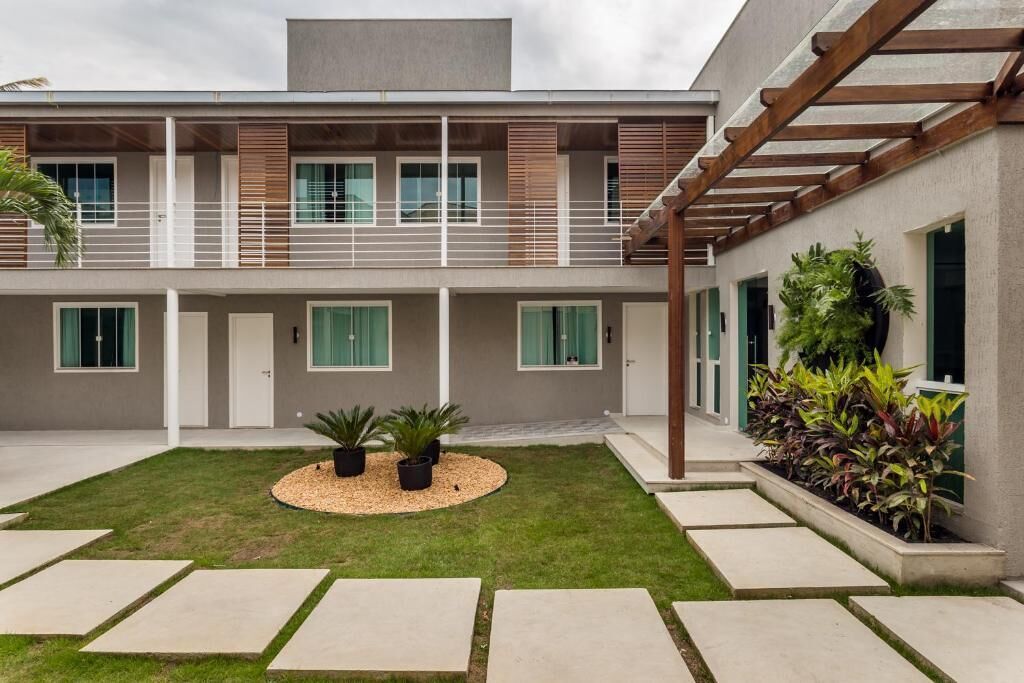 A modern two-story building with a covered patio area, a small garden with potted plants, and a concrete pathway leading to the entrance.