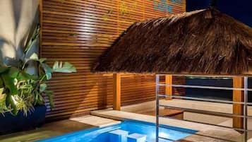 Un área de piscina moderna con un muro de listones de madera y una estructura de techo de paja.