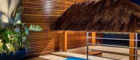 A modern pool area with a wooden slatted wall and a thatched roof structure.