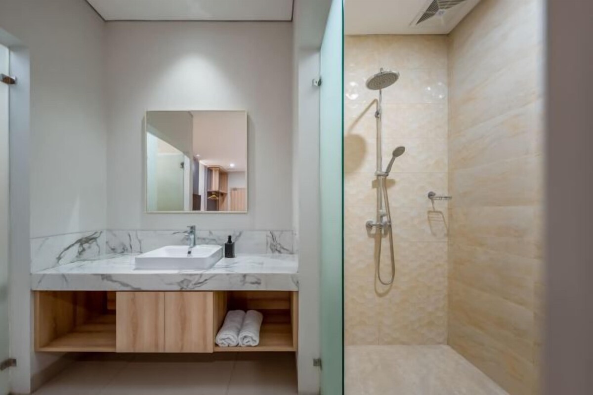A modern bathroom with a marble sink, wooden cabinetry, a glass shower enclosure, and a large mirror.