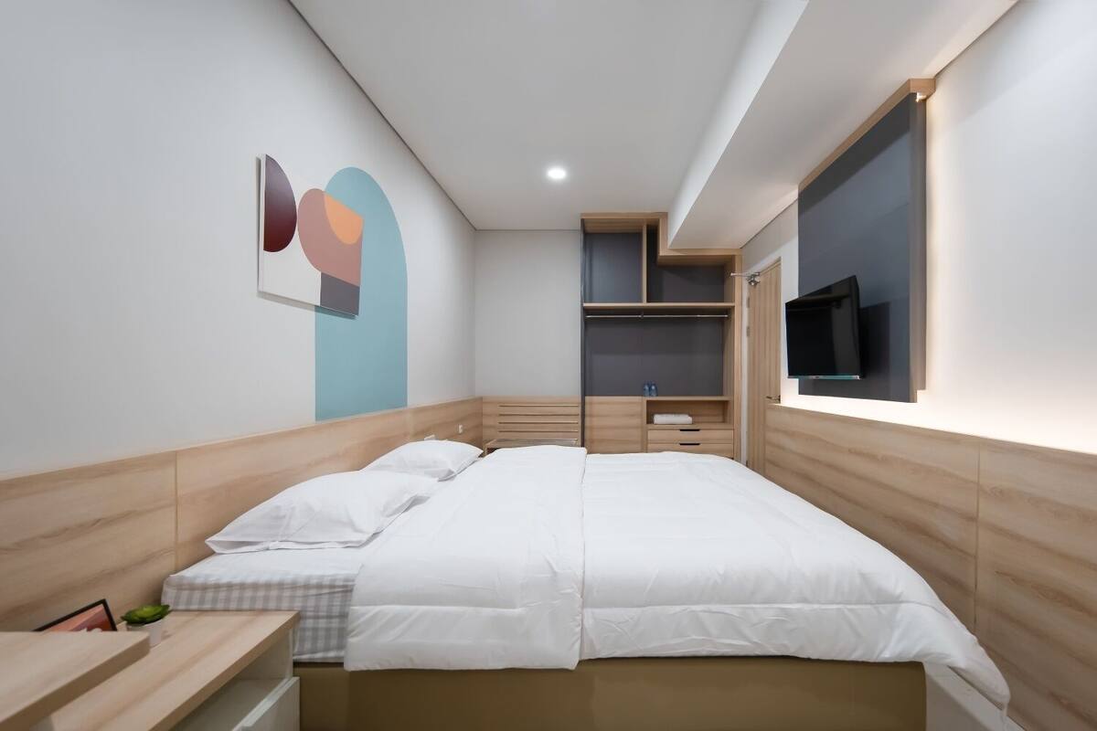 A modern bedroom with a large bed, built-in shelving, a TV, and a wall art piece.