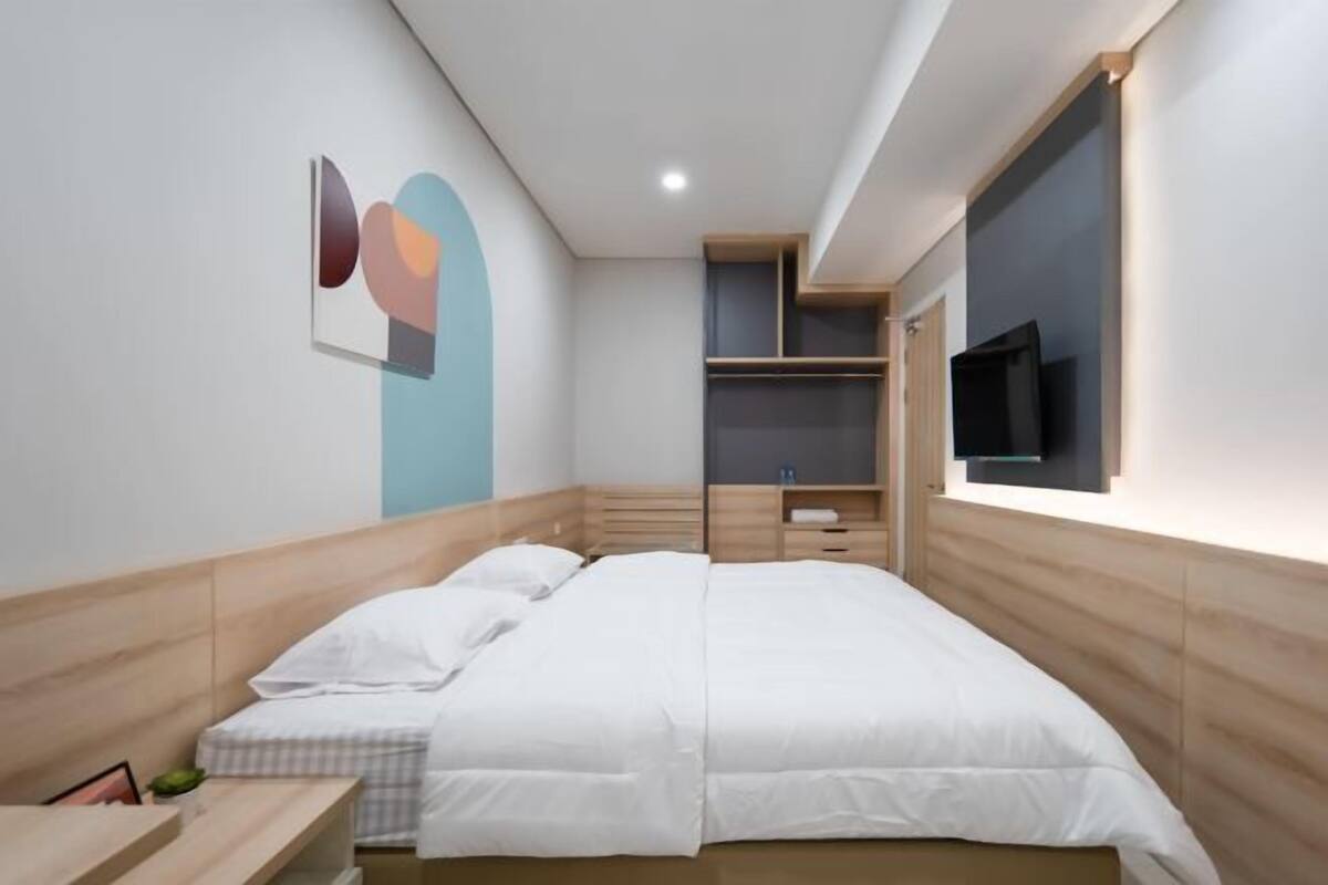 A modern bedroom with a bed, bedside tables, a TV, and built-in storage.