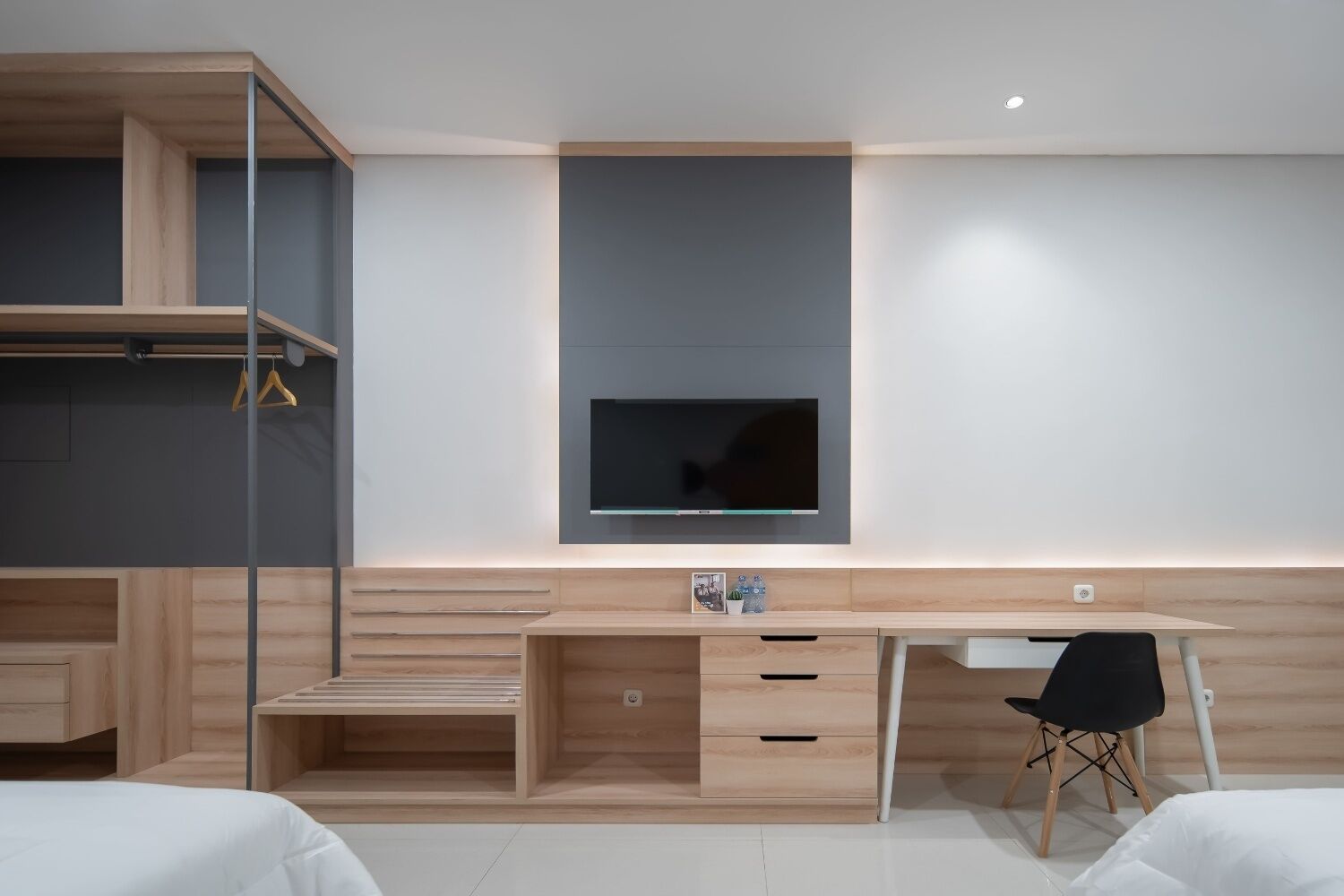 Een moderne slaapkamer met een houten bureau, een aan de muur bevestigde televisie en een bed met witte beddengoed.