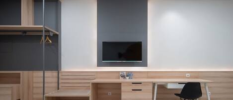 Un dormitorio moderno con un escritorio de madera, un televisor montado en la pared y una cama con ropa blanca.