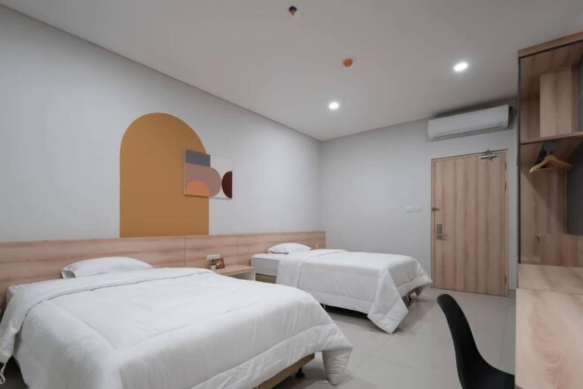 A hotel room with two beds, a wooden wardrobe, a desk, and a wall-mounted air conditioner.