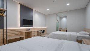 Une chambre d’hôtel moderne avec deux lits, un bureau avec une chaise, un téléviseur fixé au mur et une salle de bain visible à travers une porte ouverte.