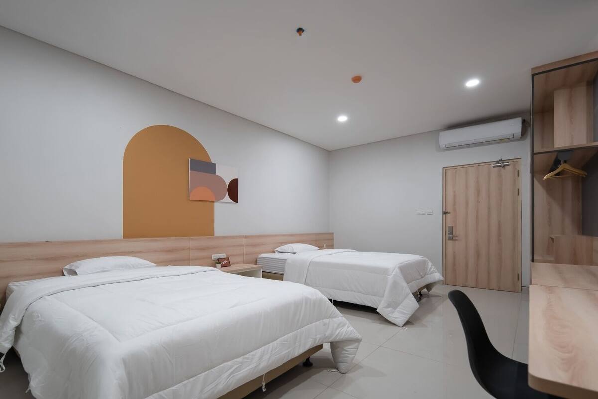 A hotel room with two beds, a wardrobe, a desk, and a wall-mounted air conditioner.