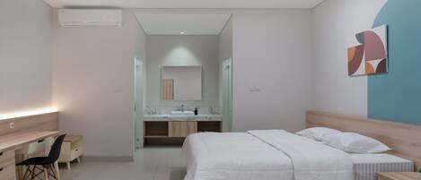 A modern bedroom with a bed, bedside tables, a desk, and a chair. There is a bathroom with a mirror and a sink.