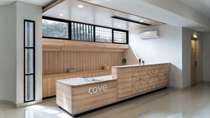 Un comptoir d’accueil portant l’inscription « cove », un mur recouvert de panneaux en bois et une grande fenêtre donnant sur des arbres.