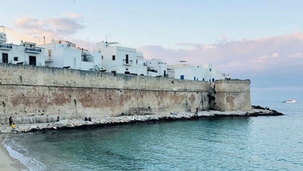 A coastal scene with a white building adjacent to a sandy beach and calm sea. - Holyday Home in Historic Center very close ti Porta Vecchia Beach  (Monopoli)