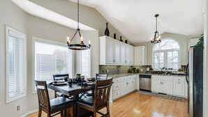 A kitchen with wooden flooring, white cabinets, a dining table with chairs, and pendant lighting.