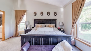 A bedroom with a large bed, two bedside tables with lamps, a bench, and a view of the outdoors.
