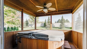 A hot tub with a wooden deck, a ceiling fan, and a view of a backyard with trees and a fence.