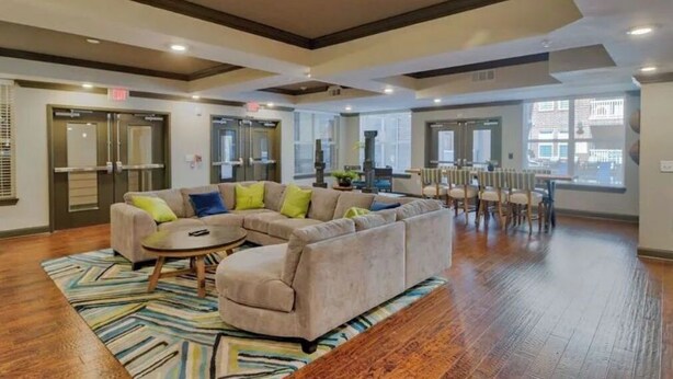 A spacious living area with a large sectional sofa, a coffee table, and a dining table with chairs. There are large windows providing natural light and a view of the city. - Cozy 1Br Near Downtown + Free Parking + Wifi+ Pool (Nashville)