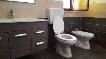 A bathroom with two toilets, a sink, and a cabinet.