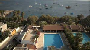 A resort with a swimming pool, lounge chairs, and a view of the sea with boats. - Eskiyali Otel (Bodrum)